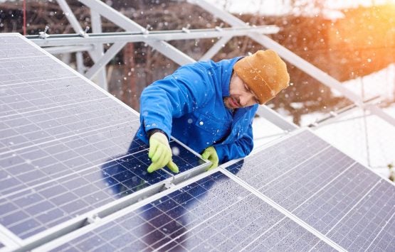 Guy with the help of tools installs solar panels in snowy weather. He is dressed in uniform and gloves Solar installation in the snow